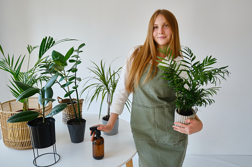 A beautiful girl takes care of plants by spraying them with water. Florist works and sprays aquatic plants. Happy and smiling florist watering plants