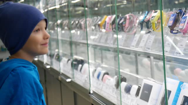 A cute happy boy walks along the showcases with digital goods and examines them carefully
