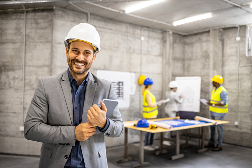 Portrait of civil engineer in business suit and hardhat holding tablet computer at construction site.