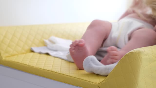 Mom dresses her little tender baby in a white bodysuit. Baptism of an infant.