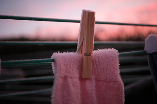 Close up of a frozen pink sock on a washing line during sunrise on a winter morning.