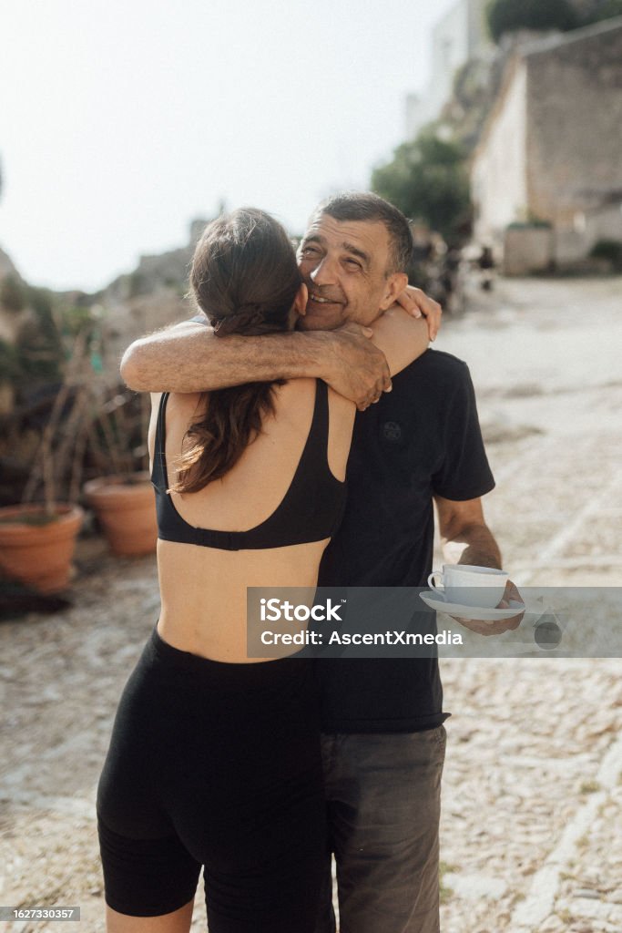 Father hugs adult daughter outside He is casually dressed and enjoying a coffee Wealth Stock Photo