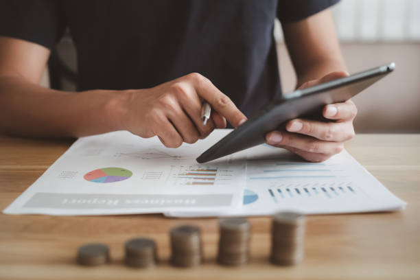 istock Businessman using applications for financial and accounting information. Man is touching black tablet screen on desk with stack coins at office. Saving money and planning for business growth concept 1627347591