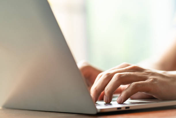 istock man is using a laptop to search for business information, stocks on desk and communicate using social media with colleagues using the Internet. Closeup hands typing keyboard and free copy space 1627349744