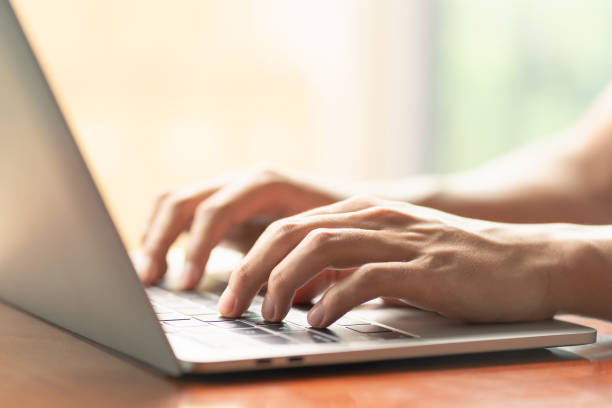 istock man is using a laptop to search for business information, stocks on desk and communicate using social media with colleagues using the Internet. Closeup hands typing keyboard and free copy space 1627350668