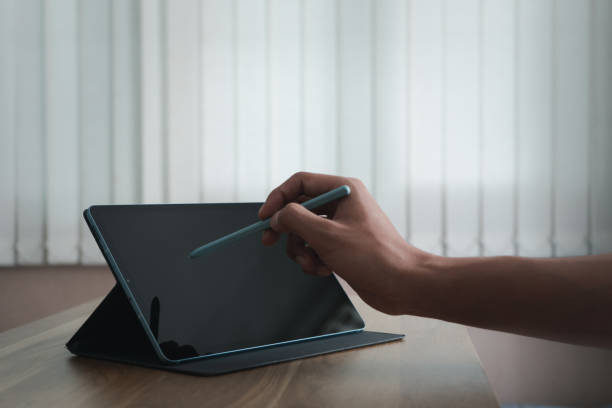 istock Man hand is using a pen to write to the tablet screen on wooden desk at workspace room. Technology and design concept. Screens can be switched to other types of ads. Sell products or other promotions 1627358393