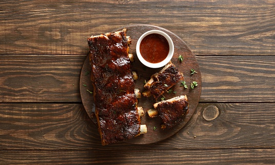 Barbecue pork ribs with sauce on board over wooden background with free space. Top view, flat lay