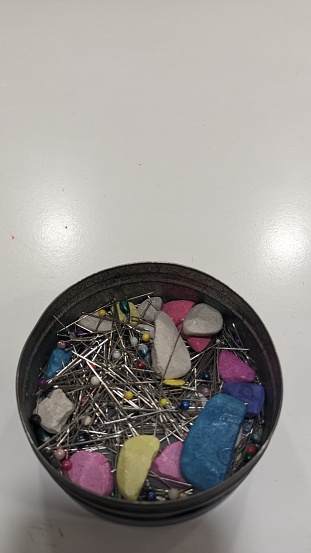Multi-colored bars of soap, chalk and needles stand in a tin can on a white table where clothes are sewn