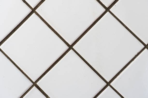 Old white ceramic wall tile pattern for decoration. Close-up vintage wall with bathroom ceramic white square diagonal tiles with defects fading.