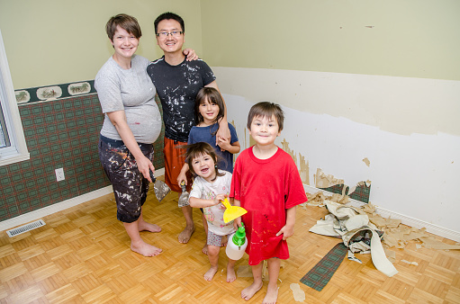 Portrait of Chinese father, pregnant caucasian mother and three kids removing wallpaper to prepare the bedroom for the new baby to come