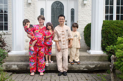 Portrait of happy multiracial family and pregnant mother posing in front porch of house in traditional chinese clothing during summer day