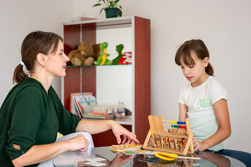 Female child psychologist working with a little elementary girl in a bright office