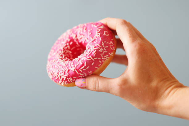 istock Female hand with manicure pink donut holding a donut 1627476955