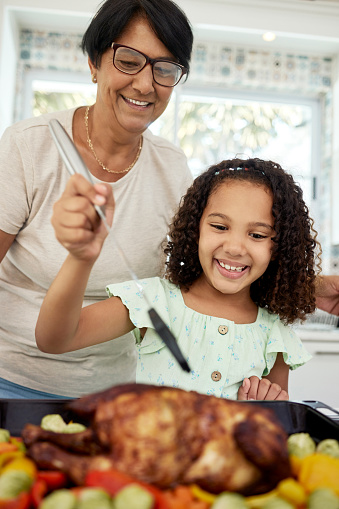 Kitchen, food and a grandmother cooking with her grandchild in their home together for thanksgiving. Children, love and a roast with a senior woman preparing a meal with a girl for healthy nutrition