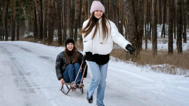 istock Happy cheerful girls riding on sleds while her sister is pulling her in forest. People playing outdoors, winter holidays and vacation, active leisure. 1627535039