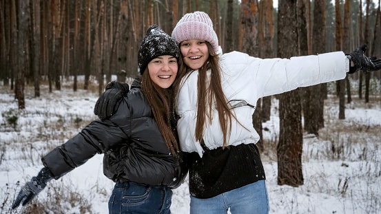 Two happy teenage girls laughing and cheering because of the first snow. People playing outdoors, winter holidays and vacation, active leisure