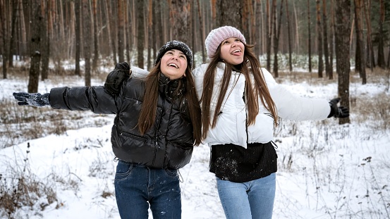 Portrait of happy laughing teenage girls enjoying snow falling in winter forest.