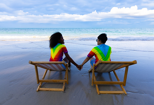 They are a lovely LGBTQ  couple hand to hand relaxing on the beach. two females lying on the sun bed  at the beach