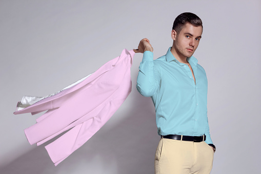 A man in a pink suit and a fashionable pink shirt isolated on a gray background.