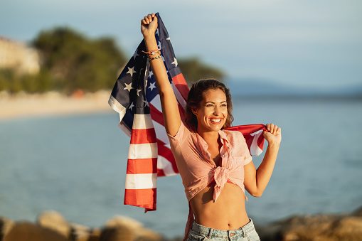 Attractive young woman with American national flag enjoying a relaxing day on the beach.