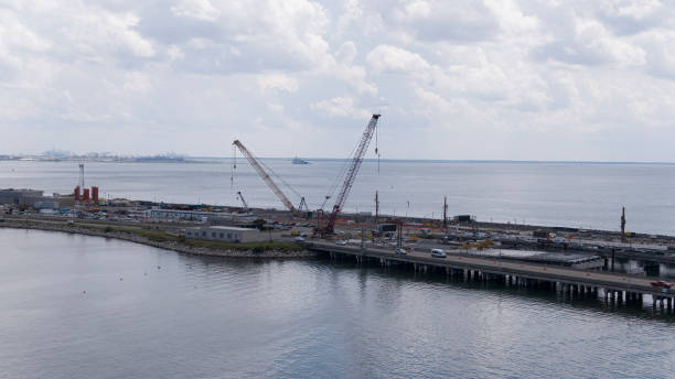 istock Engineering works on river creek under cloudy sky: Bridge construction with gantry cranes in water surroundings of Hampton Roads Beltway, VA. Aerial view 1627556382