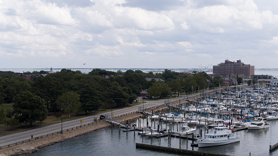 Coastal road surrounded by trees leading to harbor with boats and jetties. Cloudy sky along the waterfront in Fort Monroe, Hampton, Virginia