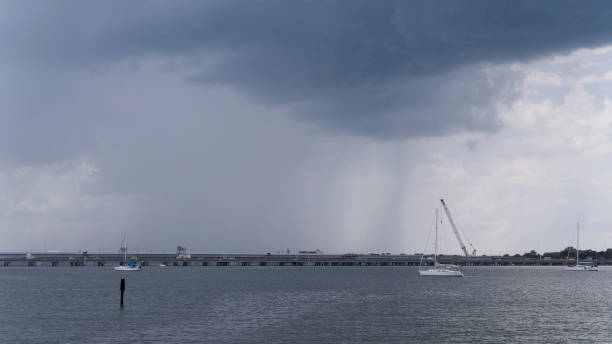 不吉な異常気象が橋の建設現場の上から始まります。遠くのフィーバスのスカイライン、バージニア州ハンプトンローズ。 - sailboat pier bridge storm ストックフォトと画像