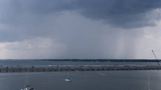 天候の変化と雨が建設された橋の上から始まります。バージニア州ハンプトンローズの曇りの不吉な空を背景に川に乗るヨット。航空写真 - sailboat pier bridge storm ストックフォトと画像