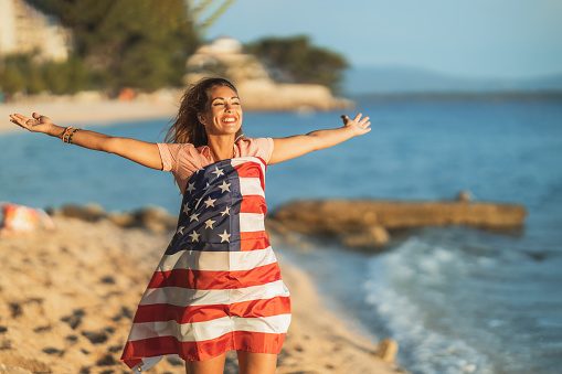 Happy young woman with US national flag spending a relaxing day on the beach.
