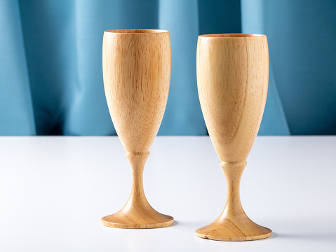 Two wooden wine glasses on a white table against a blue silk curtain.