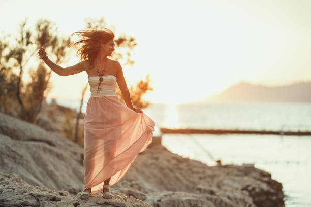 An attractive young woman is having fun and dancing while enjoying a summer vacation at the wonderful seaside.