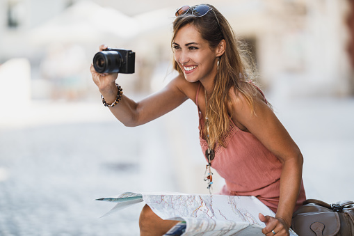 Shot of a young smiling woman taking photos while exploring a foreign city.