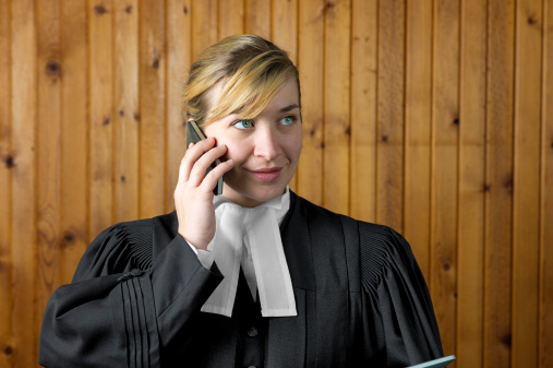 A woman barrister or lawyer takes a call on her mobile or cell phone while wearing traditional court robes.  These robes are similar throughout the British Commonwealth.