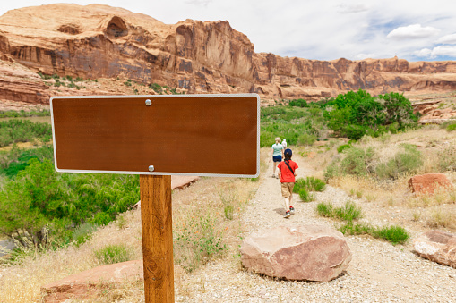Empty Tourist Sign in Utah Desert with Tourists Hiking on the Background. Mock up for any Text