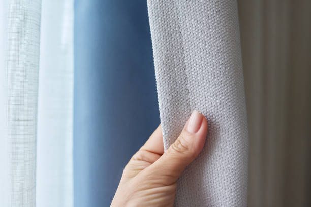 istock Woman's hand showing light gray curtain on blue opaque lining, fabric blackout 1627577298