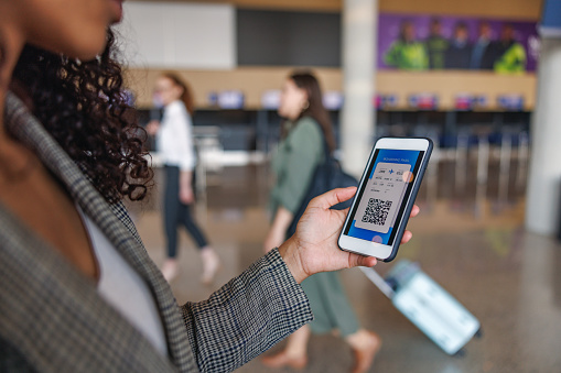 Close-up shot of a Latin-American business woman looking attentive at her digital boarding pass on her phone to check her departure date and wait for her upcoming flight surrounded with other passengers.