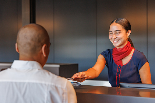 Waist-up of a mature Latin-American man being helped by a young and attractive Mixed-Race stewardess with his check-in and baggage.