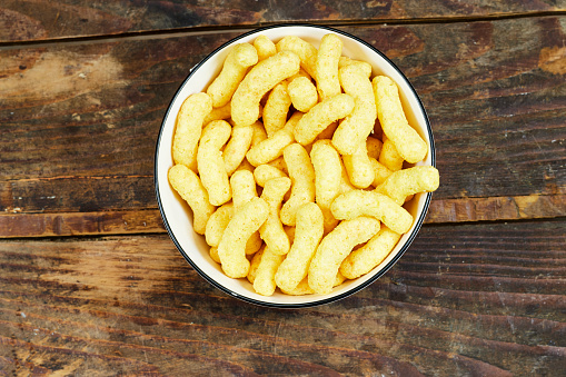 Peanut flips, in a ceramic bowl on wooden table . Also known as Bamba, peanut puffs or snips, is a puffed, peanut-flavored corn snack
