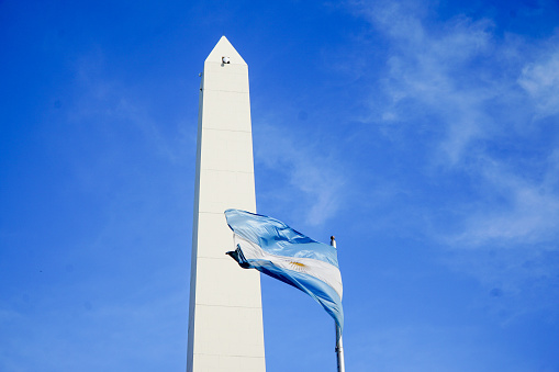 Argentinian republic iconic image. The obelisk and the argentinian flag waving in a blue sky.