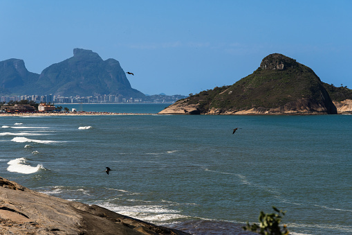 Macumba Beach and Recreio dos Bandeirantes in Rio de Janeiro, Brazil. Pedra do Pontal and Pedra da Gávea in the background. Beach on the west side of town. Sunny day and people on the beach.