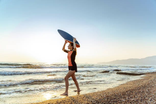 istock Young woman running on the beach, while holding a skimboard over her head 1627692202