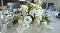 istock Dolly shot of wedding table decoration with bouquets of fresh white tender flowers with greenery, wine glasses on the background camera moving slow motion. 1627754342