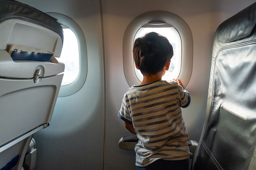 Child in the looking out the airplane window traveling on summer vacation