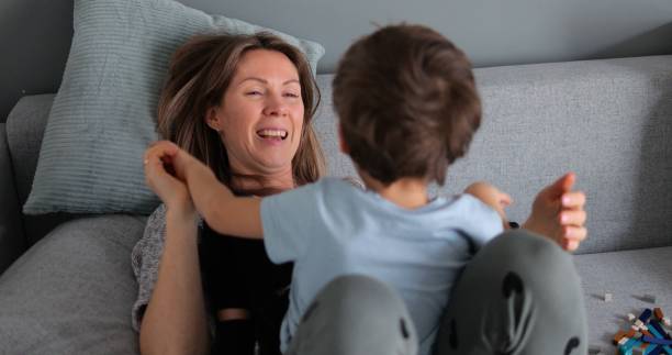 istock Middle age beautiful mother smile and play with son while lie on sofa at home. 1627787751