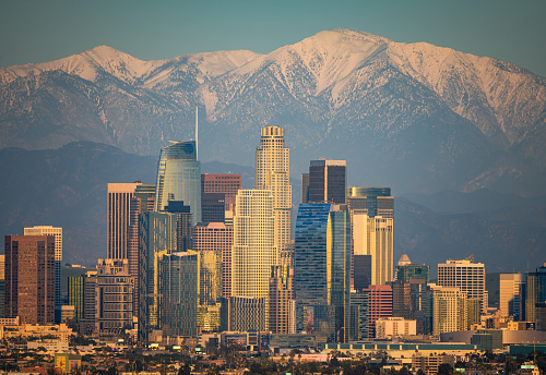 Skyline of Los Angeles with snow-capped mountain in background at sunset.