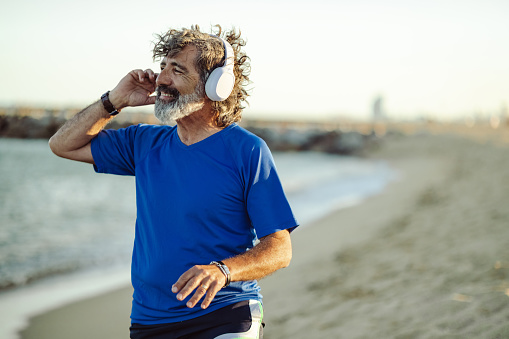 Senior man with wireless headphones standing on the beach and enjoying the moment