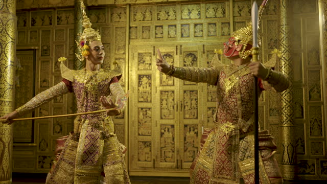 Khon or traditional Thai classic masked from the Ramakien action of dance with fighting position by human and red giant in front of Thai painting as background in public place.
