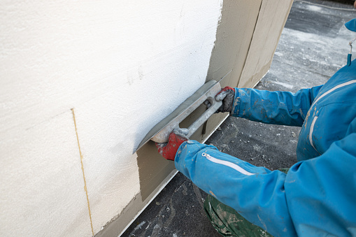 Builder plastering the wall with a spatula, fiberglass mesh, after insulating the house