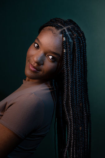 Studio portrait of beautiful young woman with braids in her hair looking at camera. Isolated on dark cyan background.