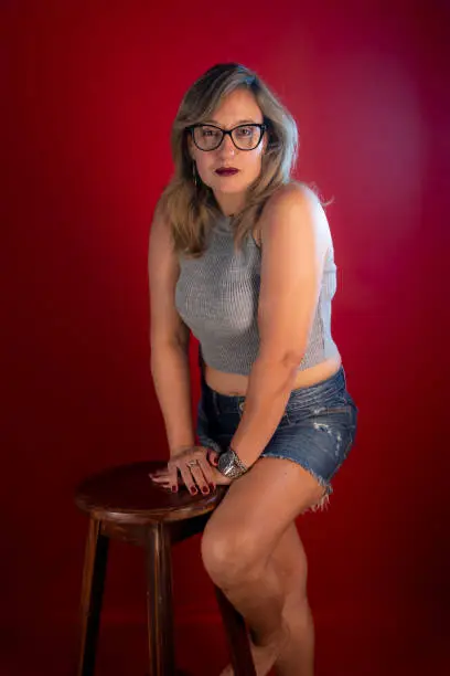 Photo of Beautiful Caucasian mature woman leaning on a stool posing for the camera.